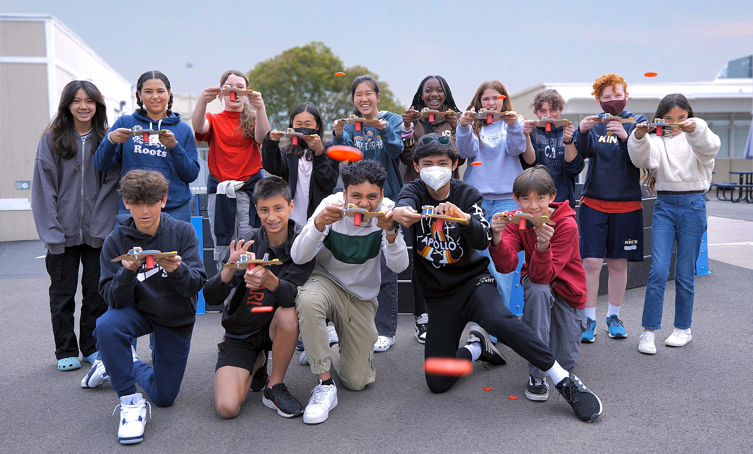 Photo of a Dozen Children Outside their School Launching Discs at the Camera