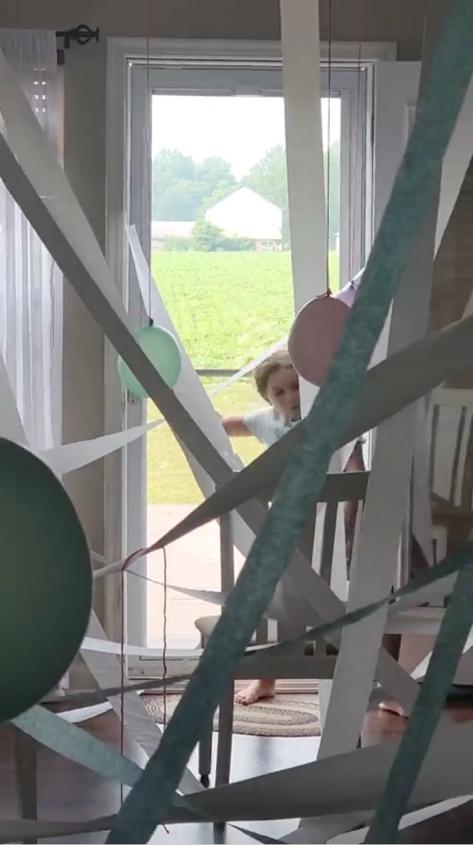 A child is walking through a doorway into a maze made with toilet paper and balloons.